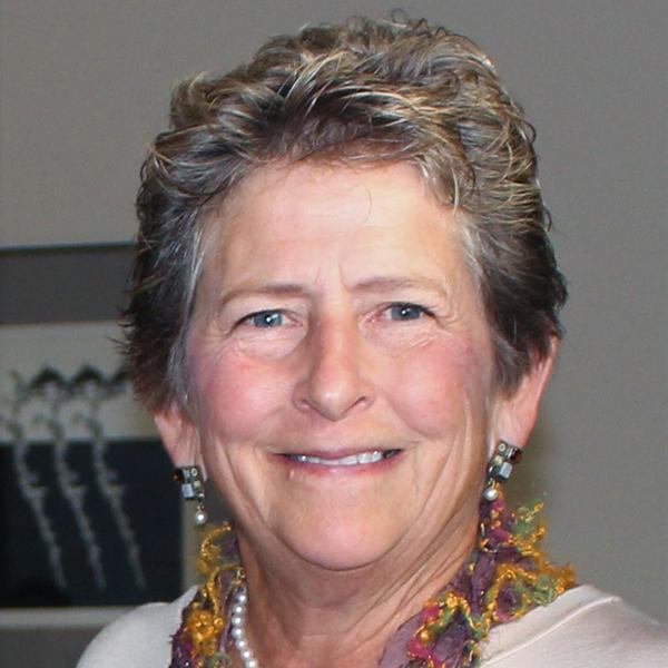 A smiling woman with short grey hair, wearing earrings and a colorful scarf, posing for the camera.